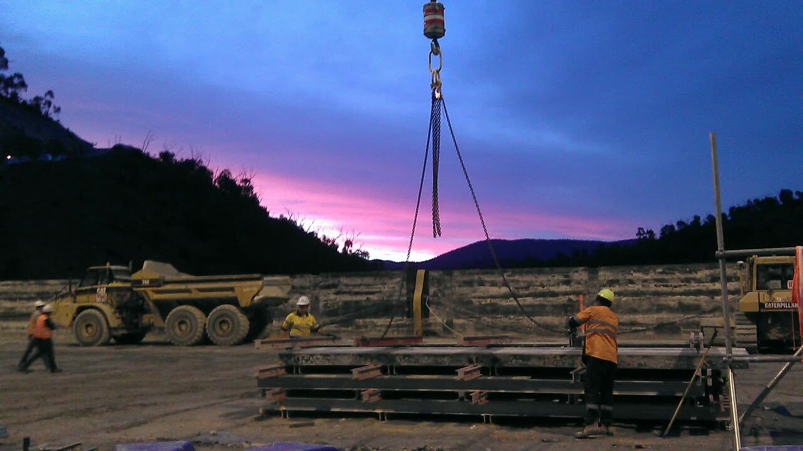 Chain sling on the crane hook at dusk with crew working below